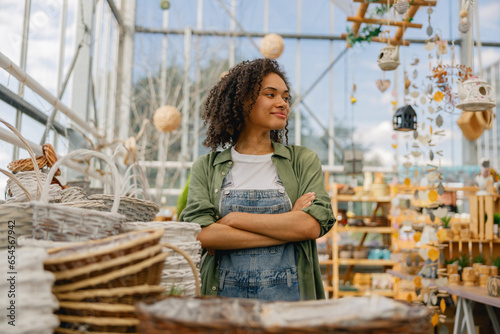Smiling female garden shop seller standing on flower store background. Gardening concept
