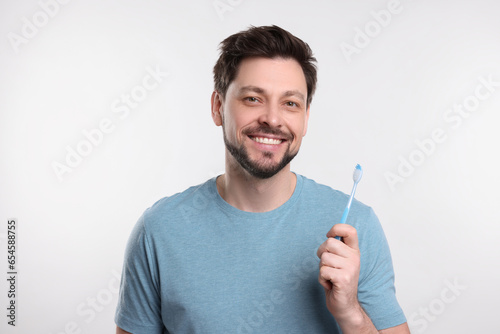 Happy man holding plastic toothbrush on white background. Mouth hygiene