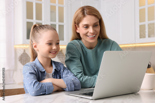 Happy woman and her daughter with laptop at white table indoors © New Africa