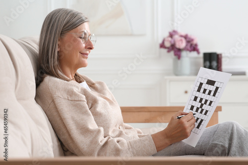 Senior woman solving crossword on sofa at home photo