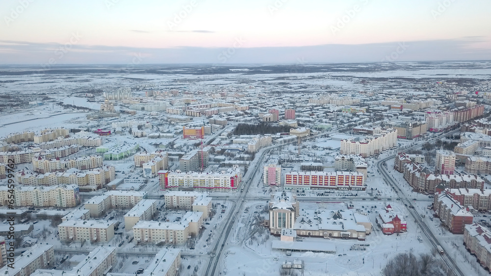Top view of city on background of hills in winter. Clip. Aerial view of modern city with colored buildings and snow-covered roads. Panorama of city with horizon on winter day