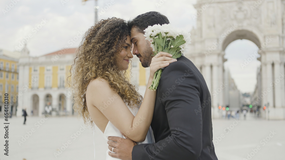 Beautiful couple of lovers tenderly embrace on street. Action. Elegant couple in beautiful outfits are gently embracing. Couple in love in beautiful outfits hugs on city square