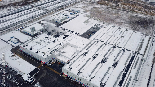 Winter view from the drone to the factory. Creative. A huge fenced building in the winter time next to which cars drive.