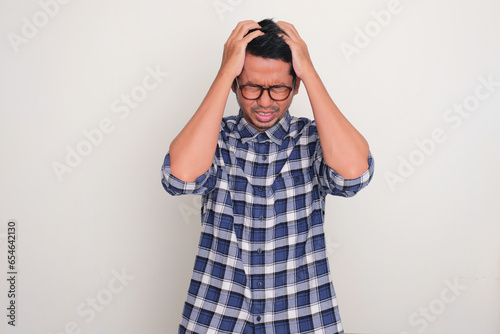 Adult Asian man facing down with hands grabbing his hair showing stress expression photo