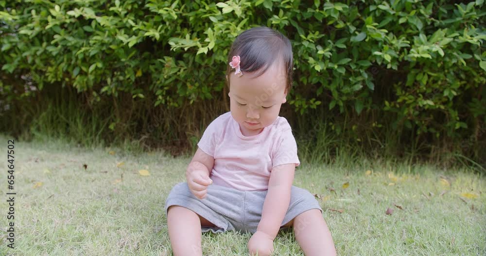 Portrait little cute baby toddler girl sitting on green grass lawn and hand touching playing learning explore grass enjoy lifestyle at nature park garden home in summertime Portrait little cute baby toddler girl sitting on green grass lawn and hand touching playing learning explore grass enjoy lifestyle at nature park garden home in summertime