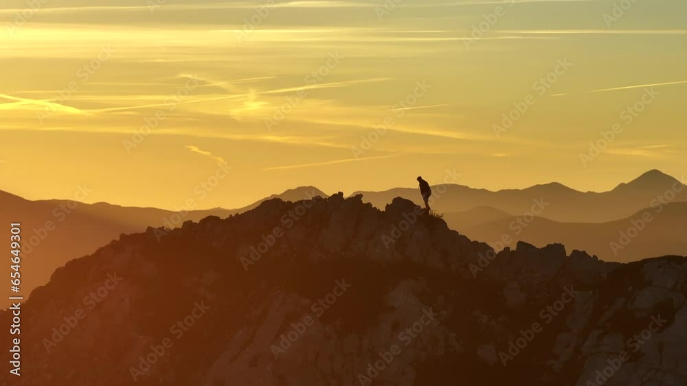 Aerial view of a mountaineer walking along a ridge at the top of a mountain with the sun in the background in a beautiful sunrise in the early hours of the day in the Pyrenees, Spain Aerial view of a mountaineer walking along a ridge at the top of a mountain with the sun in the background in a beautiful sunrise in the early hours of the day in the Pyrenees, Spain
