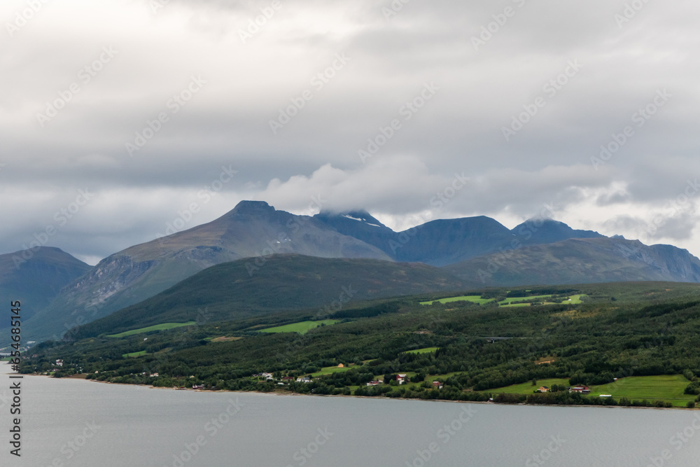Verdant mountain landscape. Clouds on peak of the mountains. Houses on the shore line. Atlantic ocean.
