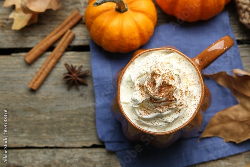 Mug of pumpkin spice latte with whipped cream  ingredients and dry leaves on wooden table  flat lay. Space for text