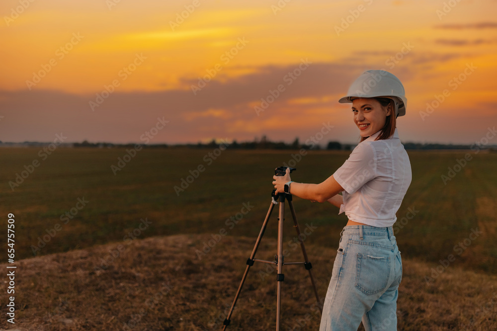 female engineer surveyor in a white helmet with a tripod in the field studying the location for the construction of a building