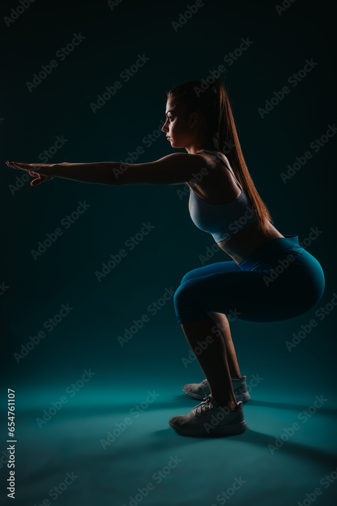 Confident woman in dark studio, doing intense workout, showcasing muscular physique, inspiring fitness goals.