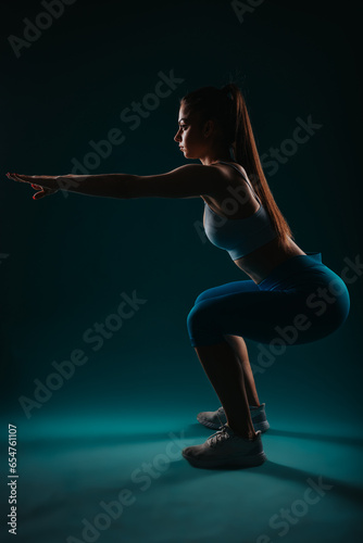 Confident woman in dark studio, doing intense workout, showcasing muscular physique, inspiring fitness goals.