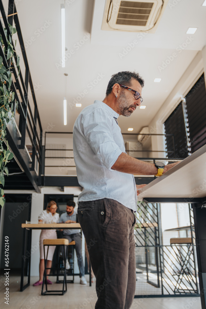 © qunica.com - Low angle of businessman working on lap top while standing in front of high working desk.