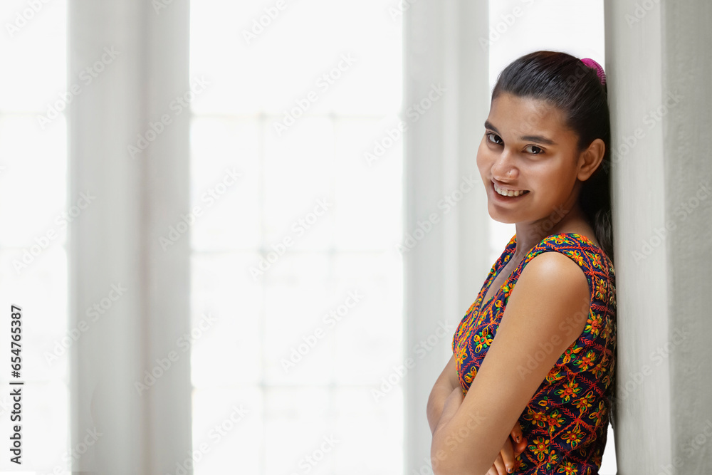 Portrait of a happy Indian teenager girl leaning on white wall, Indoors Portrait of a happy Indian teenager girl leaning on white wall, Indoors