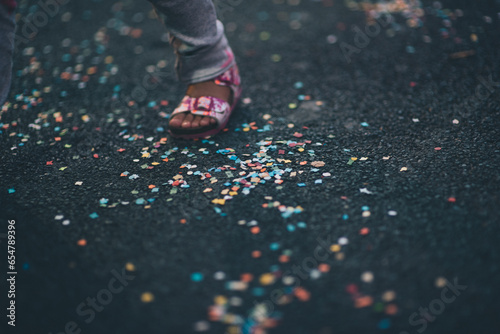 A child's foot in a pink sandal, on the ground, among confetti..