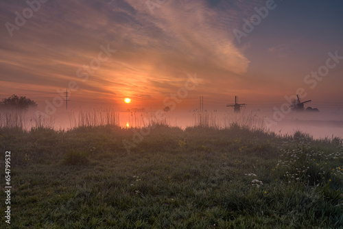 Foggy morning during the sunrise in the Munnikenpolder in Leiderdorp with the siloute of the windmills photo