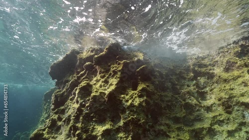 Underwater crag with seawaves in sunbeams, underwater seascape of Mediterranean Sea. Sea waves crashing against coastal rock on blue water background, Slow motion  photo