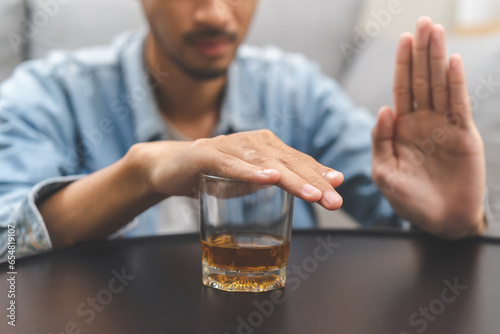 Alcoholism, depressed asian young man refuse, push out alcoholic beverage glass, drink whiskey, sitting alone at night. Treatment of alcohol addiction, having suffer abuse problem alcoholism concept. photo