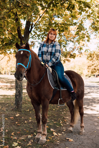 A woman sits on top of a horse. Horse riding in the autumn park