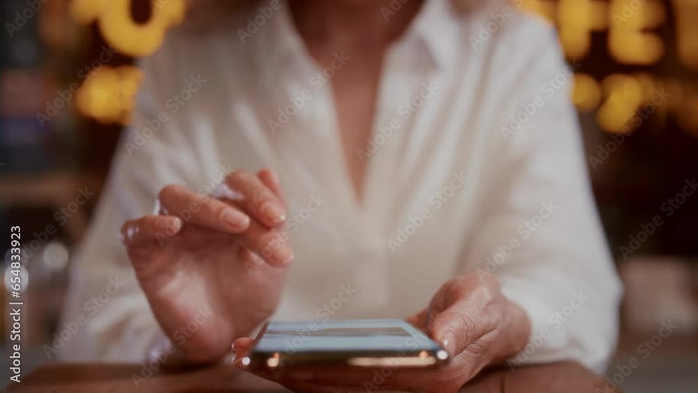 An old woman will scroll the photo on her smartphone with her hands. Senior female touches the phone screen with her fingers. Sitting in a cafe, using a mobile app. The concept of modern technologies