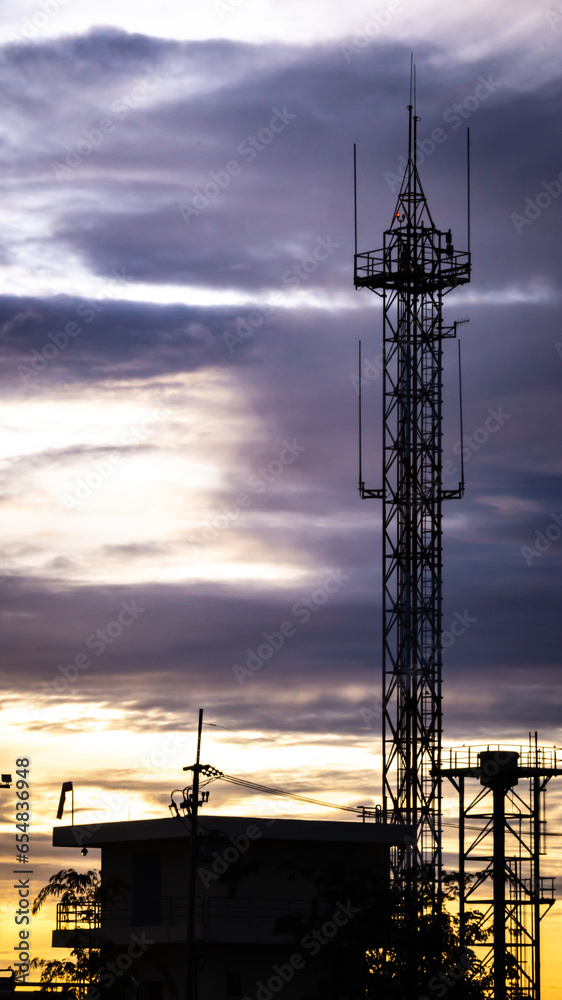 A photograph of a building, with an antenna, used for communication, with the sun in the background, in the morning.