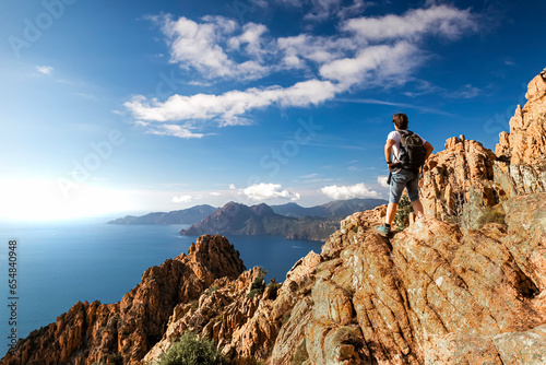 ein Wanderer steht in der Calanche einer bizarre Felsenlandschaft an der Suedkueste des Golfs von Porto im Regionalen Naturpark Korsika auf einem Felsen und schaut auf das Meer Korsika Frankreich photo