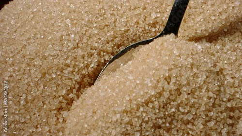 Scooping pure brown sugar with spoon. Close up slow motion sugar background. Limiting sugar is paramount to safeguarding against several chronic conditions disease, including obesity and diabetes.