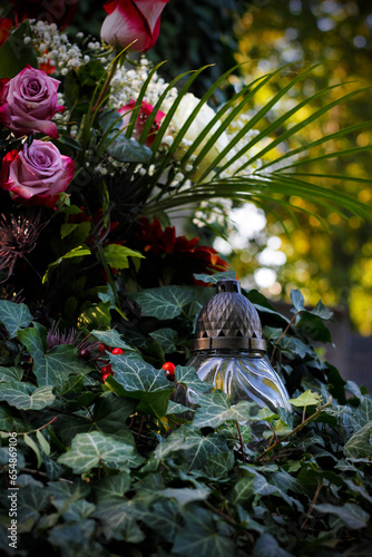 Close up of a burning candle and flower decoration on the grave overgrown with ivy. Symbol of remembrance of our deceased relatives. All Souls' Day concept. All Saints Day photo