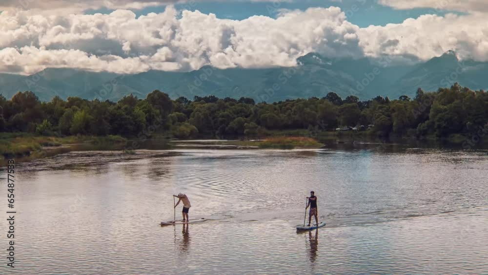 Aerial view of two adults silhouette on paddleboarding doing stand up paddle water sport activity on a wild river. Healthy lifestyle outdoor activity Aerial view of two adults silhouette on paddleboarding doing stand up paddle water sport activity on a wild river. Healthy lifestyle outdoor activity