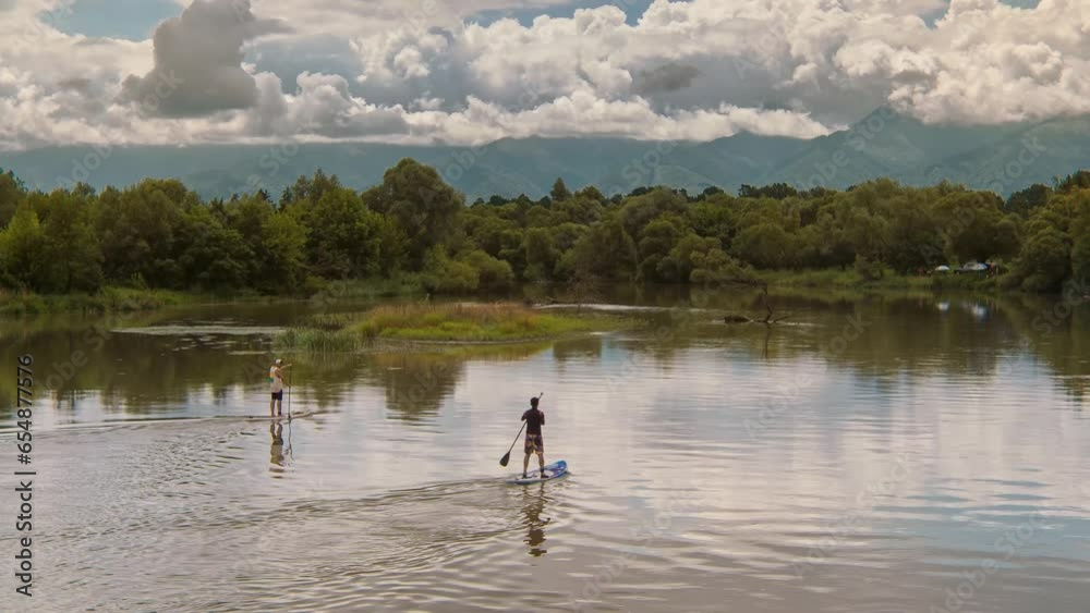 Aerial view of two adults silhouette on paddleboarding doing stand up paddle water sport activity on a wild river. Healthy lifestyle outdoor activity Aerial view of two adults silhouette on paddleboarding doing stand up paddle water sport activity on a wild river. Healthy lifestyle outdoor activity
