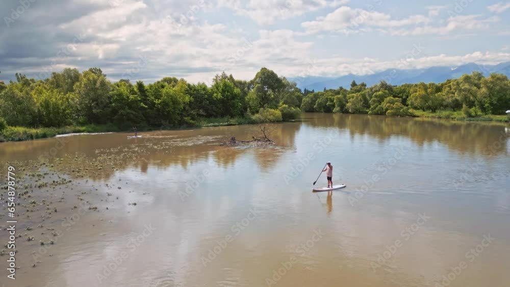 Aerial view of two adults silhouette on paddleboarding doing stand up paddle water sport activity on a wild river. Healthy lifestyle outdoor activity Aerial view of two adults silhouette on paddleboarding doing stand up paddle water sport activity on a wild river. Healthy lifestyle outdoor activity
