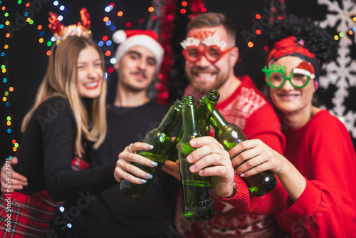 Four friends celebrating New year toasting with beer bottles. Focus on bottles