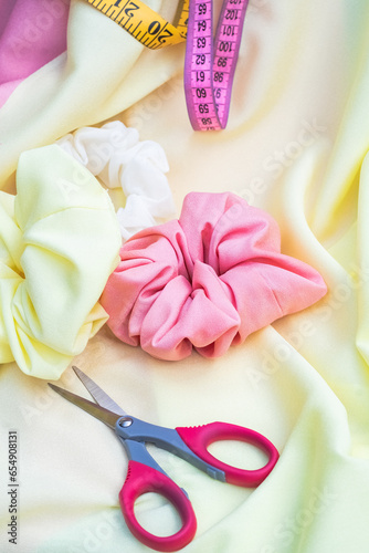 sharp red scissors  three white  yellow and pink scrunchies for hair on yellow fabric. Art and creating beauty