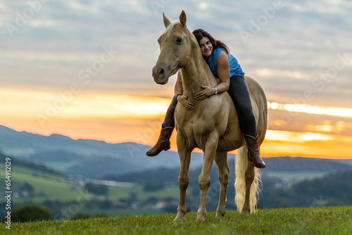 Horse and equestrian team: A young woman and her palomino caballo deporte espanol horse during sundown in summer outdoors
