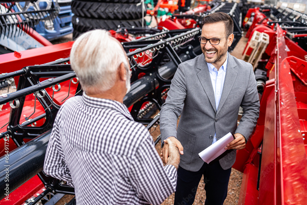 Investing in new farming equipment and agricultural machinery. Farmer and salesman shaking hands at dealership.