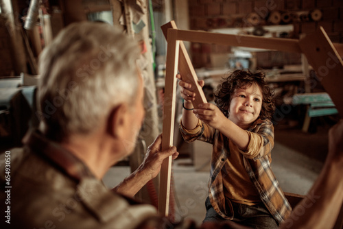 Senior male carpenter showing his grandson a wood frame in a carpentry shop