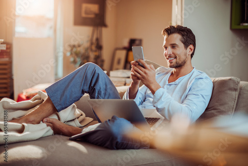Young man using his smartphone on the couch at home