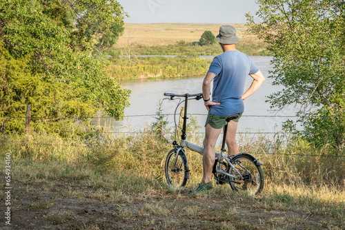 athletic senior man is looking at Dismal River after riding a folding bike in Whitetail Campground in Nebraska National Forest