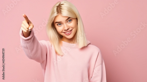 Teenager blonde girl wearing a sweater over isolated pink background surprised and pointing side