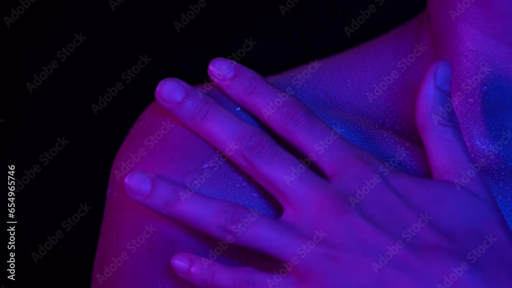 Closeup studio shot of woman touching body part in neon light, clavicle area skin after shower in water drops.
