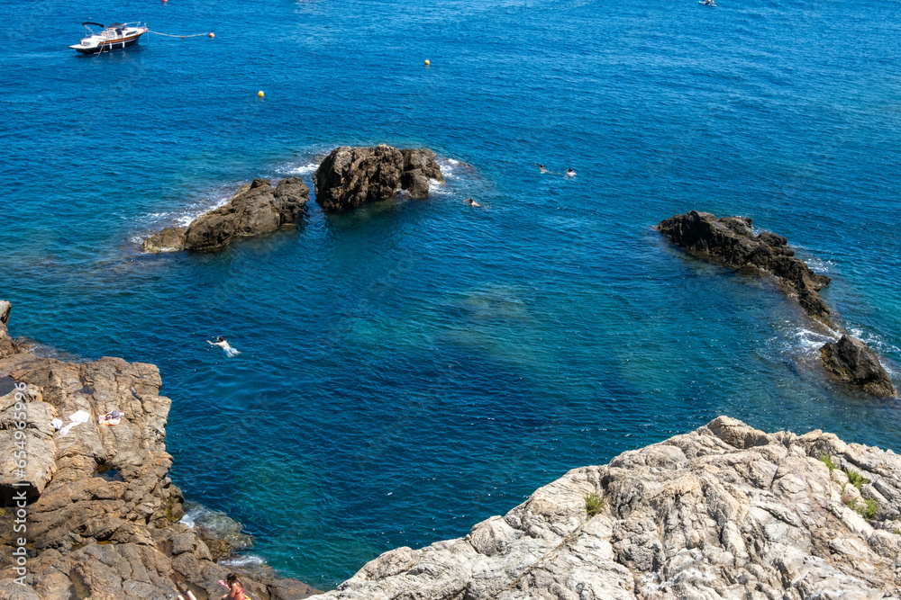 Image of the Mediterranean Sea from the Costa Brava, with tourists swimming in its crystal-clear waters.