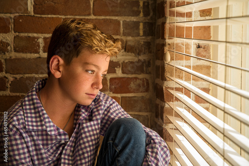 Warm natural light portrait of a boy with freckles sitting looking out of a window photo