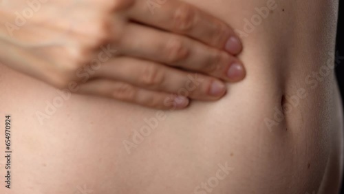 Closeup studio shot of beautiful caucasian woman body part, massaging her tummy soft skin with hand.