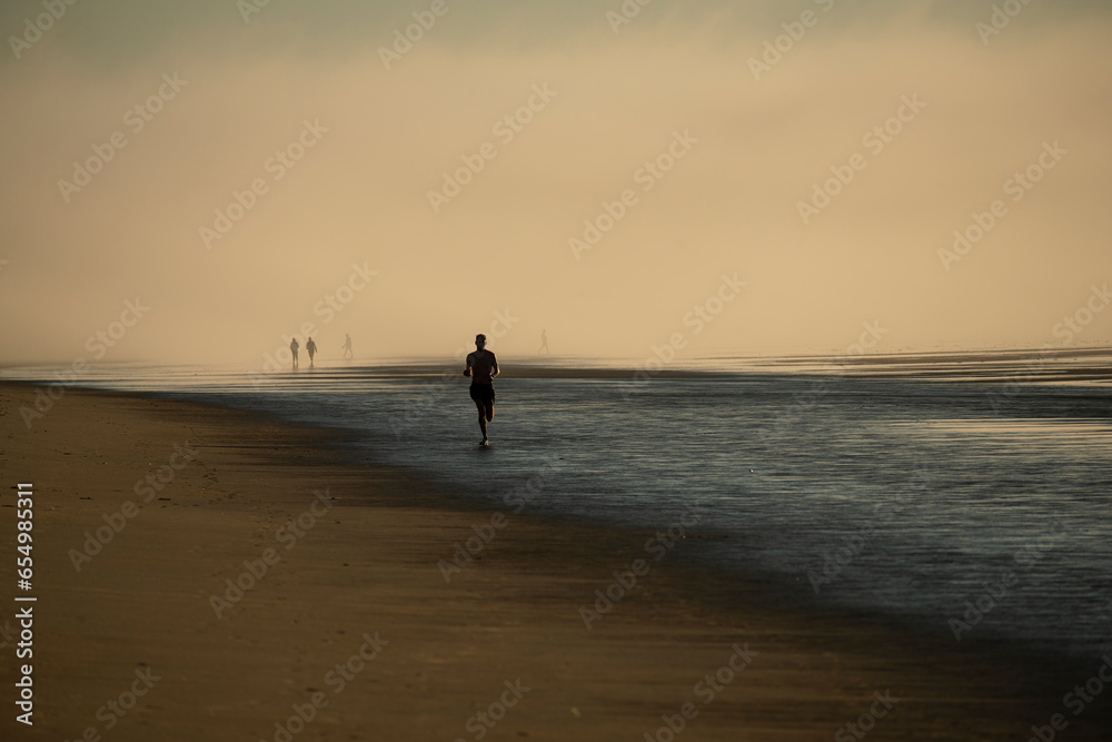 The coast of the Atlantic Ocean at dawn in heavy fog. Silhouettes of people on the shore walking and jogging at dawn. USA. Maine.