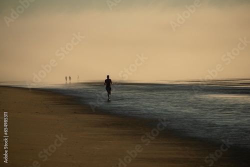 The coast of the Atlantic Ocean at dawn in heavy fog. Silhouettes of people on the shore walking and jogging at dawn. USA. Maine.
