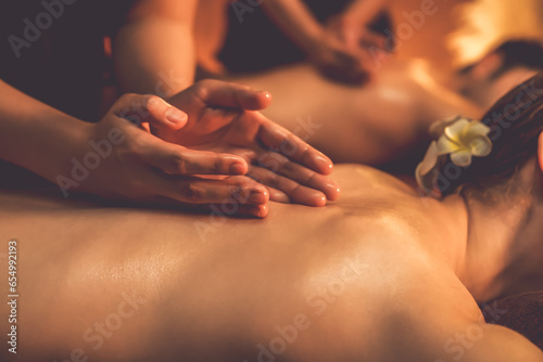 Closeup couple customer enjoying relaxing anti-stress spa massage and pampering with beauty skin recreation leisure in warm candle lighting ambient salon spa at luxury resort or hotel. Quiescent