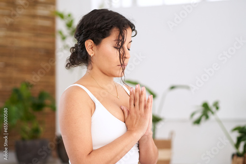 Close up Latin woman in sportswear doing yoga exercise. Young girl concentrating performing asana anjali mudra indoors. Concept of feminine wellness, meditation, body care and mental health.