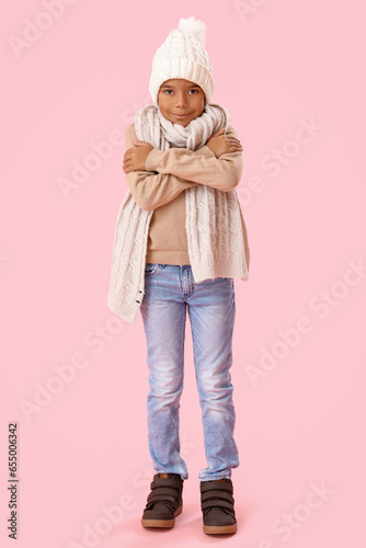 Freezing African-American boy in winter clothes on pink background