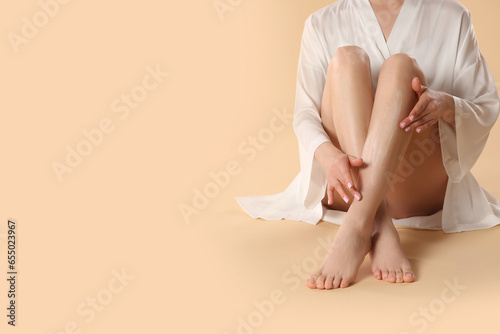 Woman applying body cream onto her smooth legs on beige background, closeup. Space for text