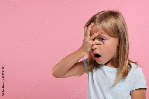 Embarrassed little girl covering face with hand on pink background. Space for text