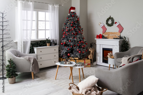 Interior of living room with Christmas tree, fireplace, grey armchairs and chest of drawers